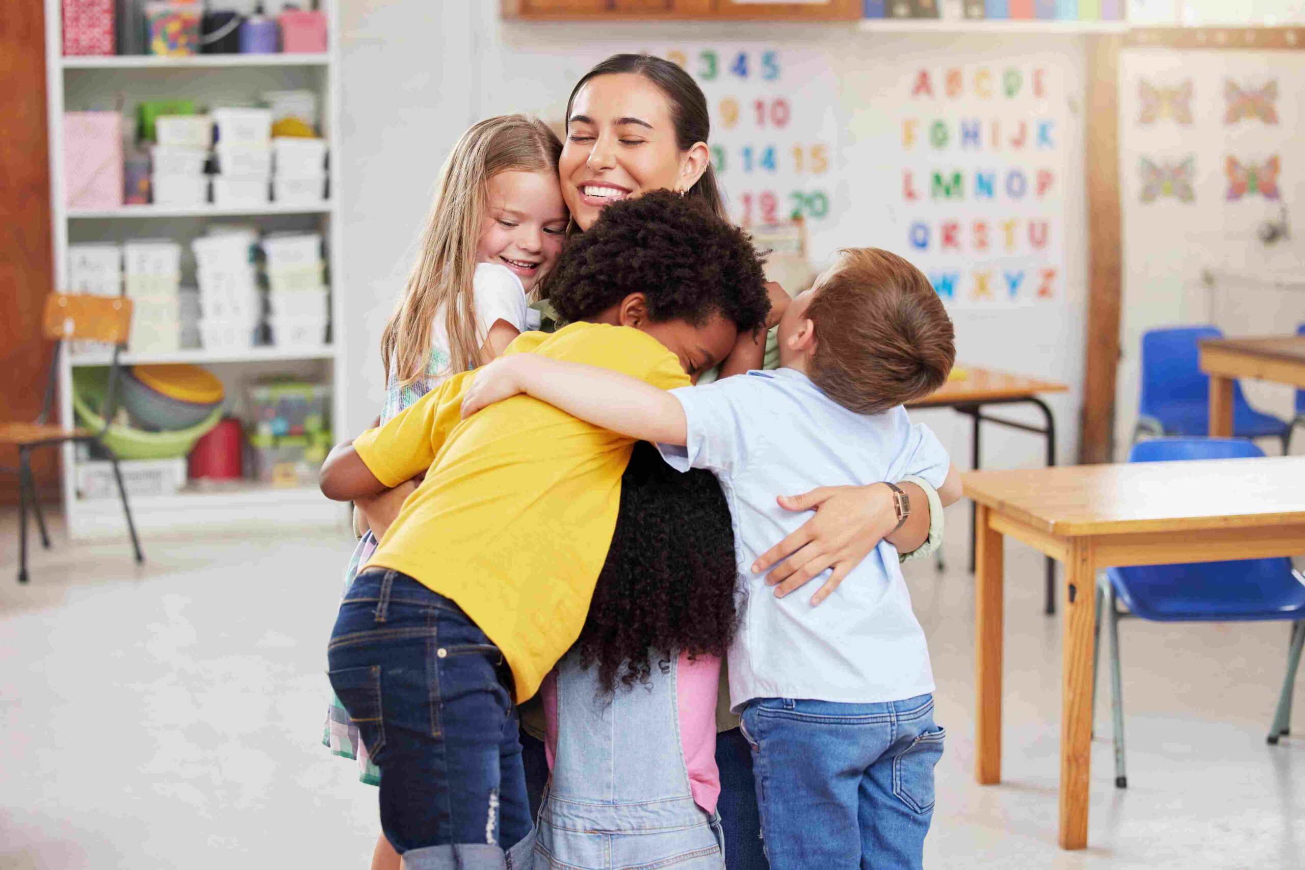 Vaspitačica grli grupu dece u učionici vrtića tokom zajedničkog trenutka